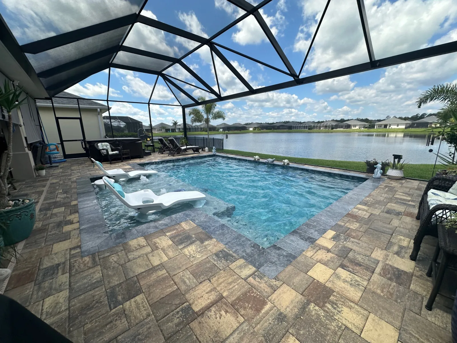 Lakefront resort-style pool with in-water loungers and paver deck by Next Level Pools and Spas — the same standard scaled to commercial and amenity spaces