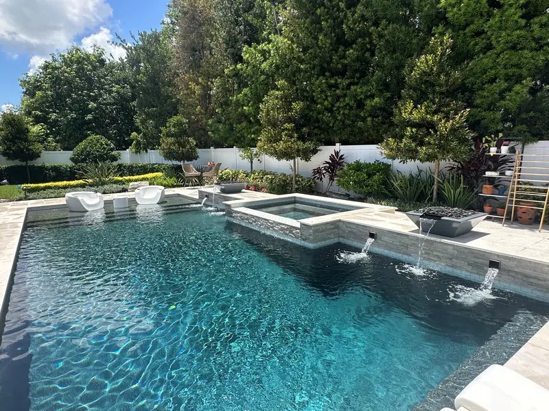 Custom pool with raised spa, stacked-stone waterline, sheer-descent scuppers, and fire bowl on a travertine deck — Next Level build in Central Florida