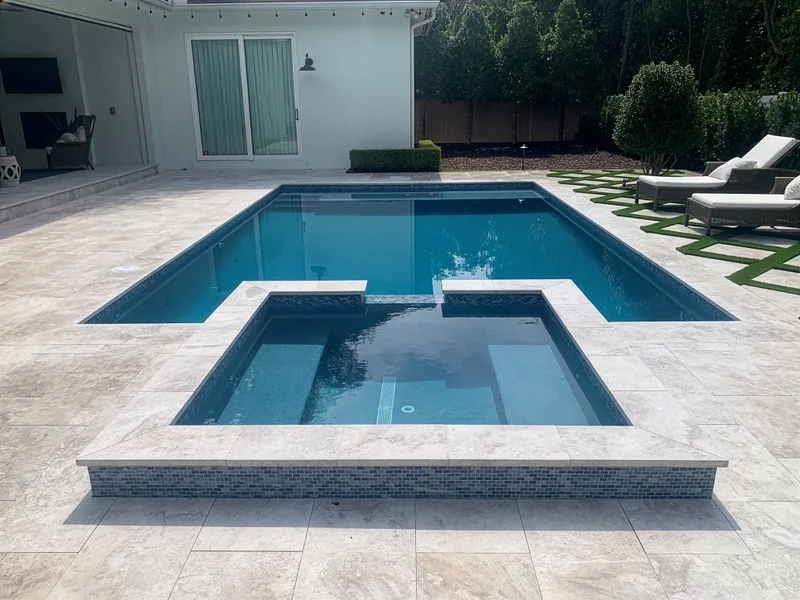 Rectangular pool with raised spa, travertine deck, and modern single-story home — Next Level build in Central Florida